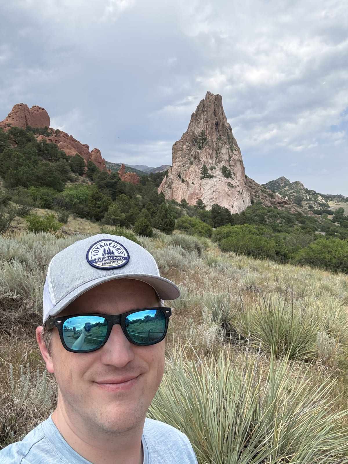 Matt in a cap and sunglasses on a hiking trail, with red rock spires behind him